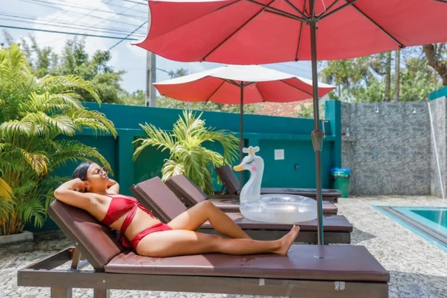Guest relaxing on a poolside lounger under a red umbrella at Tèya Beach Hotel