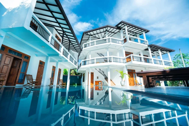 Poolside view of Tèya Beach Hotel's white two-storey building reflected in the swimming pool at midday