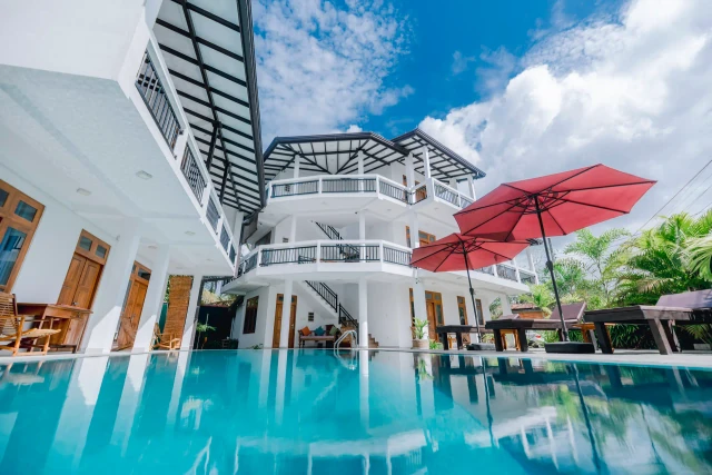 Swimming pool and sun loungers with red umbrellas at Tèya Beach Hotel