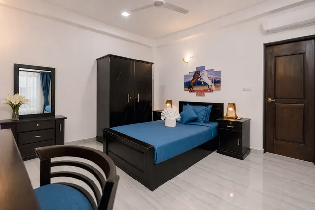 Room with blue bedding, dark wood wardrobe, and a folded towel swan on the pillow